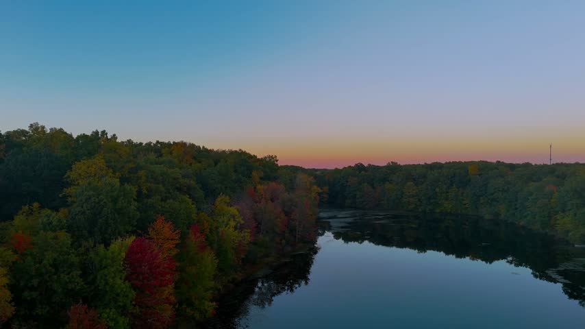 Aerial view of a reflective lake nestled among autumn woodland, with vibrant fall colors and warm sunset light creating a peaceful wilderness scene in Connecticut, USA.