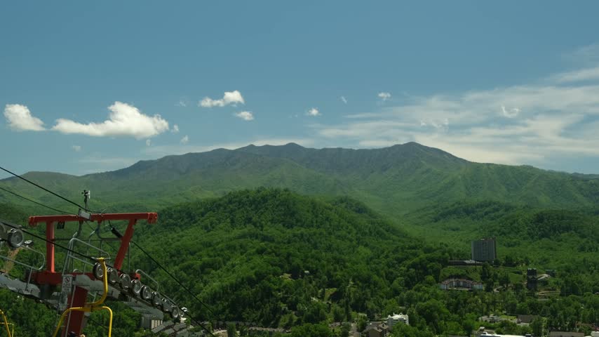 A view of the city from a ridge at midday, with green hills and blue skies near Gatlinburg and a ski lift in the foreground.
