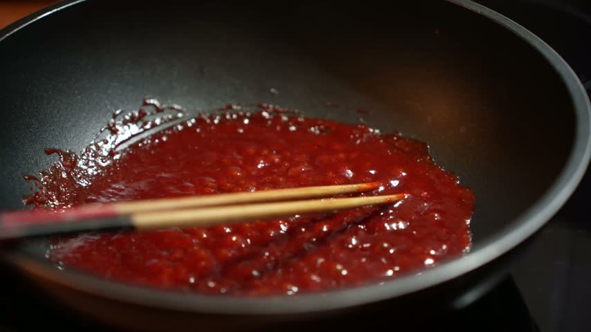 Red sauce simmers in a cooking pot on a gas stove with chopsticks resting nearby.