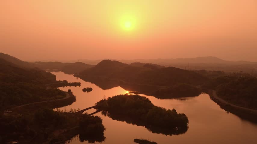 Serene Sunset Over Calm Lake Surrounded By Silhouetted Mountains And Lush Greenery