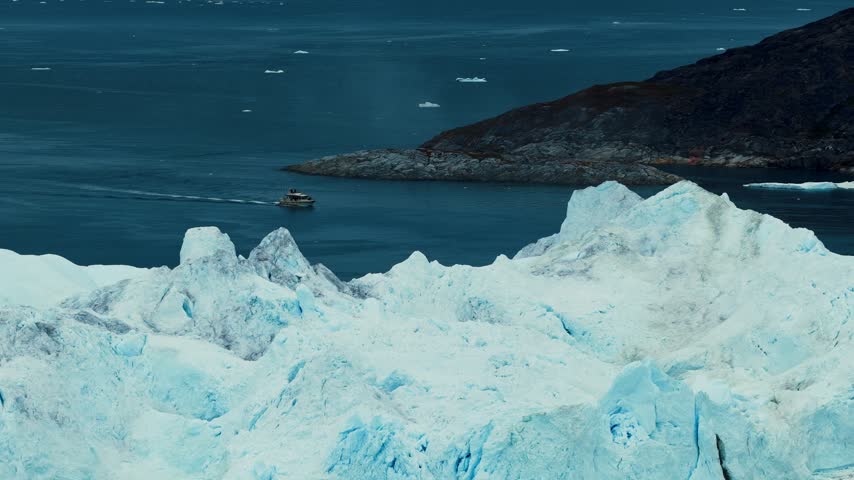 Cinematic footage of a small boat navigating between massive icebergs in the cold waters of Greenland. Mysterious atmospheric weather. 