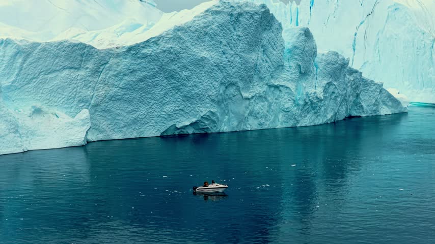 Cinematic footage of a small boat navigating between massive icebergs in the cold waters of Greenland. Mysterious atmospheric weather. 