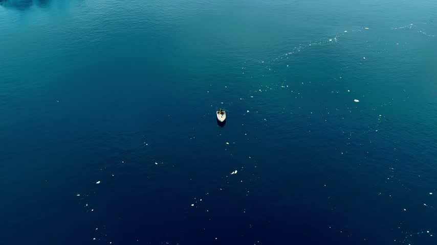 Cinematic footage of a small boat navigating between massive icebergs in the cold waters of Greenland. Mysterious atmospheric weather. 