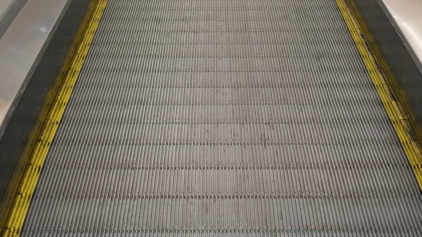 Close-up of a moving walkway or travelator with yellow safety lines inside a modern shopping mall or supermarket. Retail trade, commerce and modern infrastructure concept.