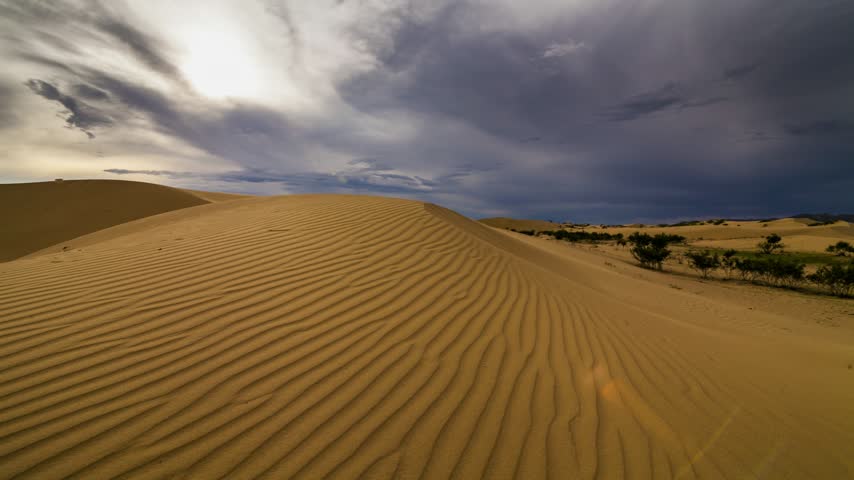 Dramatic thunderstorm clouds gathering over vast golden sand dunes in a remote desert landscape
