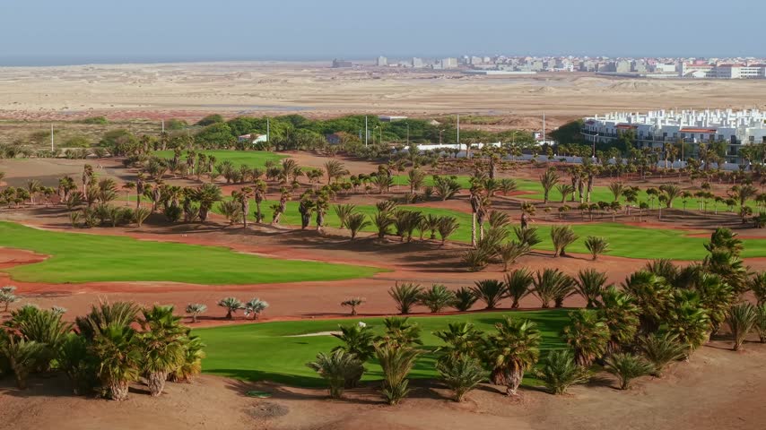 Aerial view of lush green fairways and palm trees of a golf course built in the desert terrain of Sal island, Cape Verde.