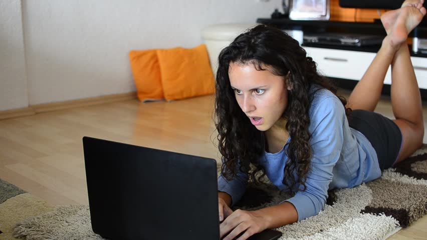 Beautiful young teen girl laying in living room with laptop