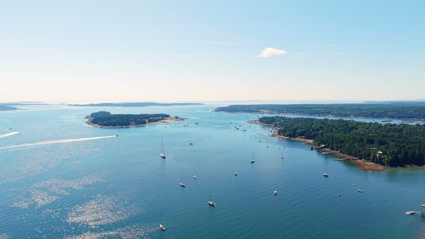 Southwest Harbor and surrounding coastal islands dotted with moored boats, captured in a high-angle aerial video on a clear sunny day on Mount Desert Island, Maine.
