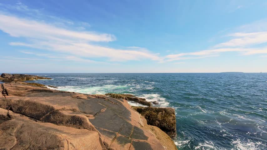 Vibrant ocean waves crashing over rocky granite shores at Otter Point in Acadia National Park, Maine, under a sunny sky.