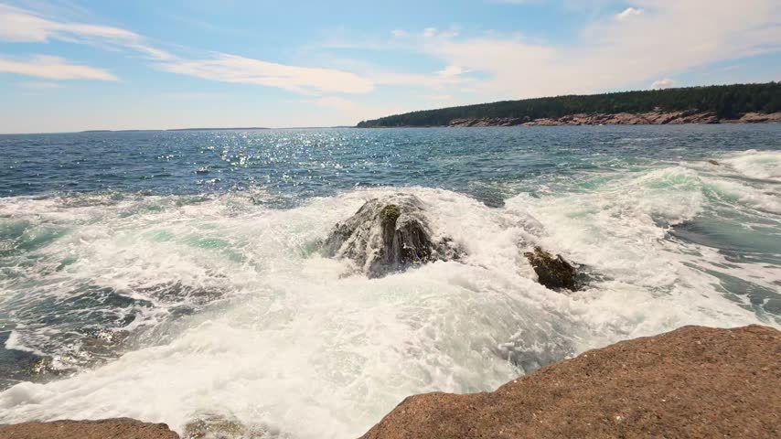 Vibrant ocean waves crashing over rocky granite shores at Otter Point in Acadia National Park, Maine, under a sunny sky.