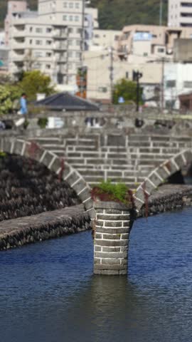 Meganebashi Spectacles Bridge, Megane bridge, stone double arch bridge over Nakashima river in Uonomachi, Nagasaki, Nagasaki Prefecture, Kyushu Island, Japan, buildings and green hills on a sunny day