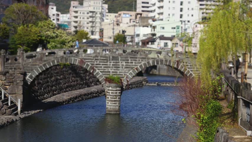 Meganebashi Spectacles Bridge, Megane bridge, stone double arch bridge over Nakashima river in Uonomachi, Nagasaki, Nagasaki Prefecture, Kyushu Island, Japan, buildings and green hills on a sunny day