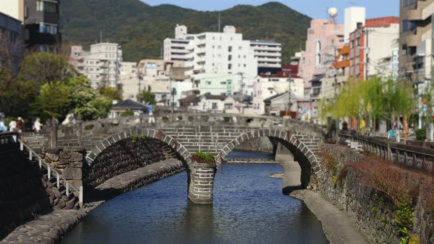 Meganebashi Spectacles Bridge, Megane bridge, stone double arch bridge over Nakashima river in Uonomachi, Nagasaki, Nagasaki Prefecture, Kyushu Island, Japan, buildings and green hills on a sunny day