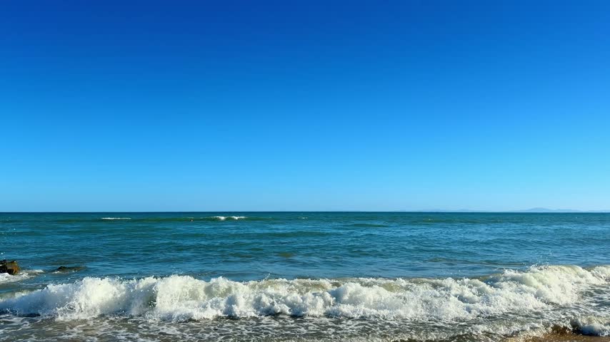 Blue ocean seascape with small waves and clear sky. Wide angle view of sea surface with mild ripples reaching the horizon under a cloudless atmosphere.