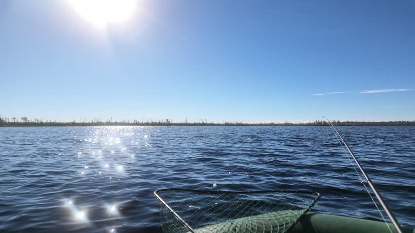 Slow smooth pan of a northern lake shore with dwarf vegetation viewed from an inflatable boat during fishing.
