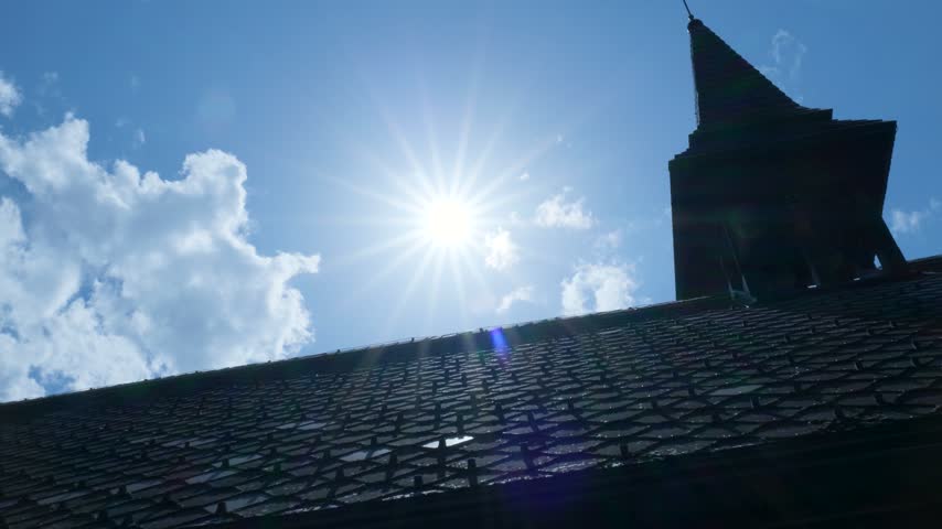 Backlit church bell tower with a rooster weather vane silhouetted against the bright sun. Switzerland