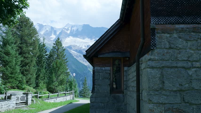 Stone church building with a panoramic view of the majestic snow-capped swiss alps in summer. Switzerland