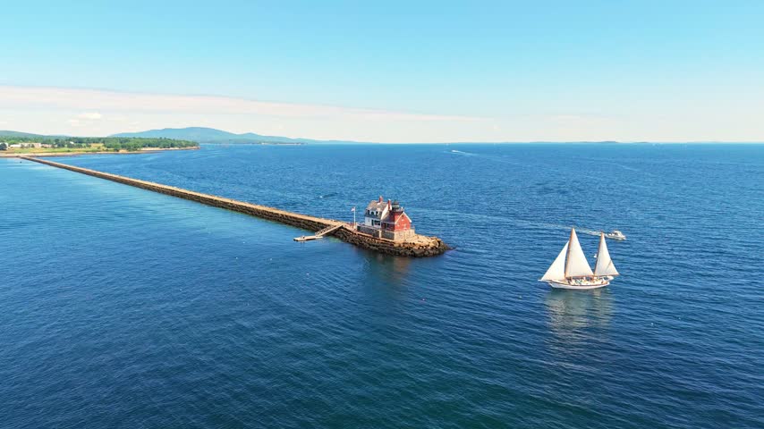 Aerial view of a two-masted schooner sailing past Rockland Breakwater Light and the long granite breakwater in Penobscot Bay near Rockland, Maine.