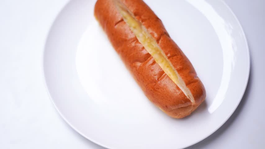 Hand Placing Jumbo Sausage into Fresh Hot Dog Bun During Homemade Hot Dog Preparation.