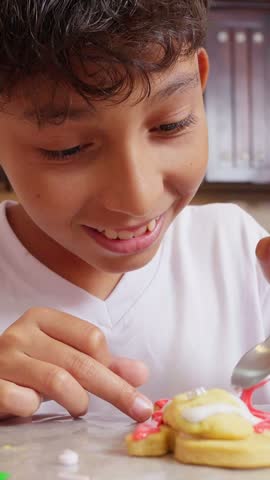Adorable young boy smiling while carefully decorating a snowman-shaped christmas cookie with colorful frosting and sprinkles, enjoying a festive holiday baking activity in the kitchen