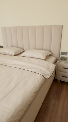Soft cream bed with pillows and upholstered headboard in a warmly lit modern bedroom interior, viewed from above