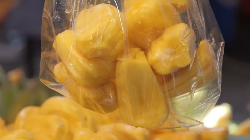 A detailed, close-up shot of bright yellow, ripe jackfruit bulbs packed inside a transparent plastic bag.