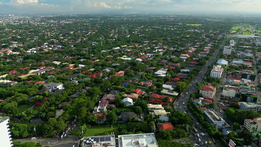 Daytime aerial drone flight toward New Alabang Village in Muntinlupa, Metro Manila, Philippines. The footage captures the leafy residential neighborhood, local streets, houses and surrounding urban la