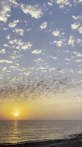 Breathtaking sunset over the sea with scattered fluffy clouds and golden sun reflection on water surface