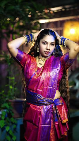Beautiful Bengali woman wearing a traditional red and purple saree posing gracefully outdoors.