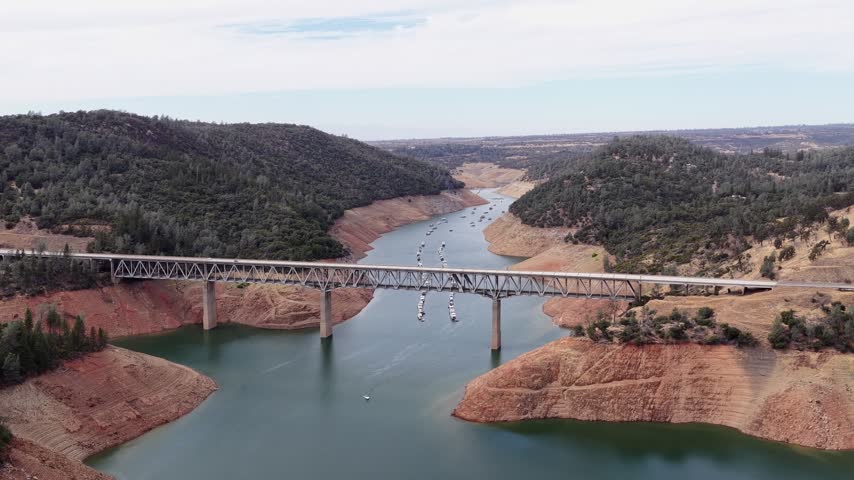 Drone push in shot towards the West Branch Feather River Bridge, revealing boats on Lake Oroville in Northern California during a severe drought with very low water levels