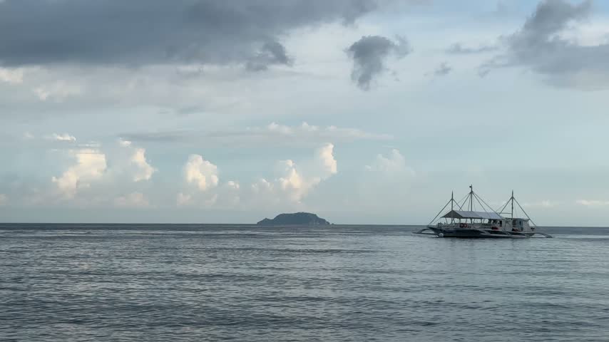 A traditional boat sailing on the calm sea near an island in the Philippines