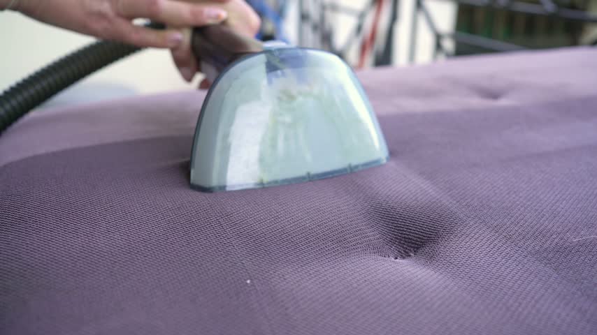 Close up of a steam cleaner vacuuming a purple sofa