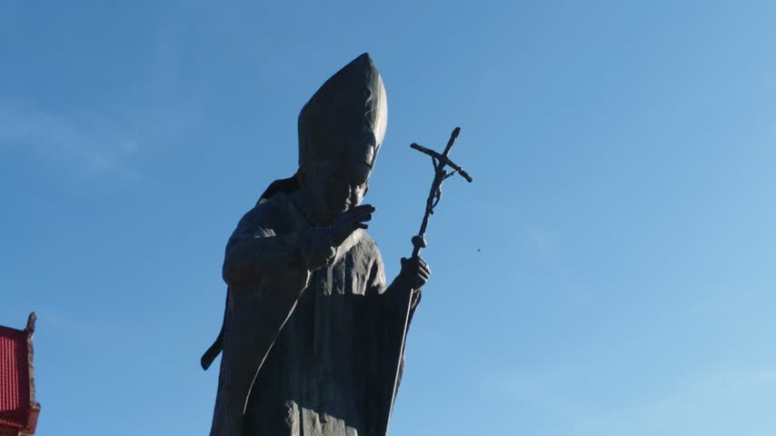Religious statue holding a cross silhouetted against the blue sky at a historic church site in Cacica, Romania.