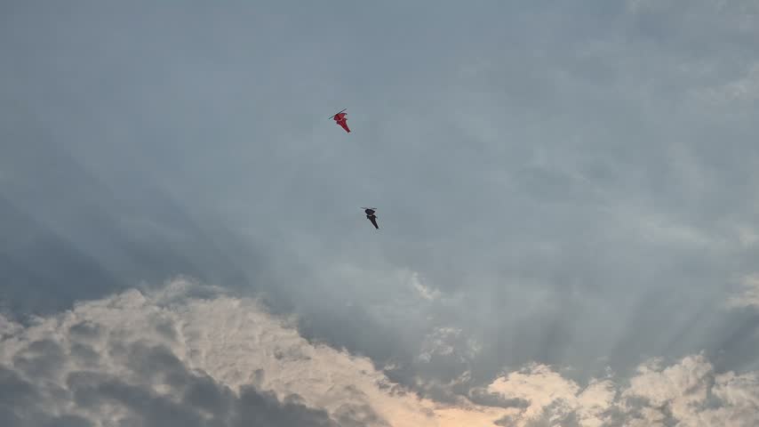 Two kites flying high in the cloudy sky with beautiful sun rays