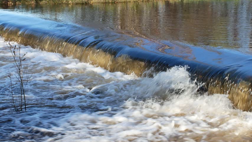 A dynamic video capturing powerful, fast-flowing floodwater rushing through the scenic Hupisaaret city park in Oulu, Finland, during a crisp autumn day.