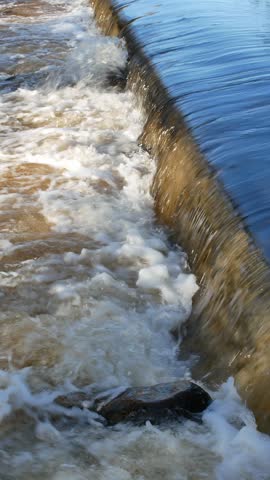 A dynamic video capturing powerful, fast-flowing floodwater rushing through the scenic Hupisaaret city park in Oulu, Finland, during a crisp autumn day.