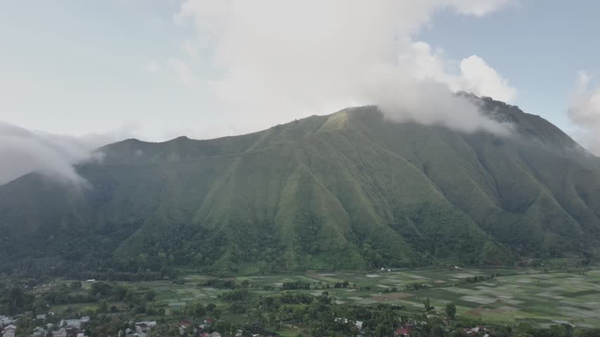 Aerial view of green mountain ridge with clouds above rural valley