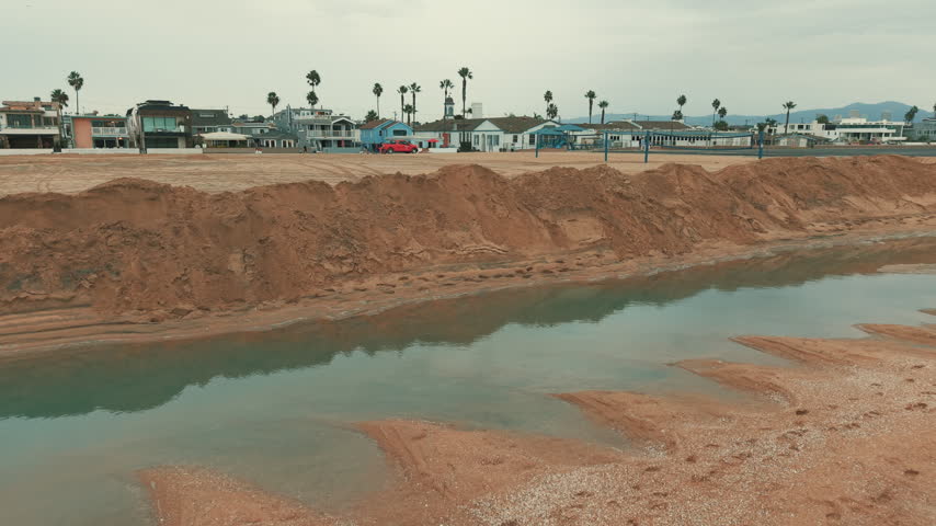 Aerial view of large sand walls and shallow floodwater near Balboa Peninsula in Newport Beach, showing coastal flood protection measures.