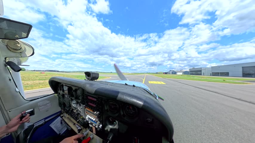 Small Cessna airplane taxiing on airport taxiway toward the runway, cockpit point of view with pilot hands, instrument panel and propeller under a blue sky with clouds