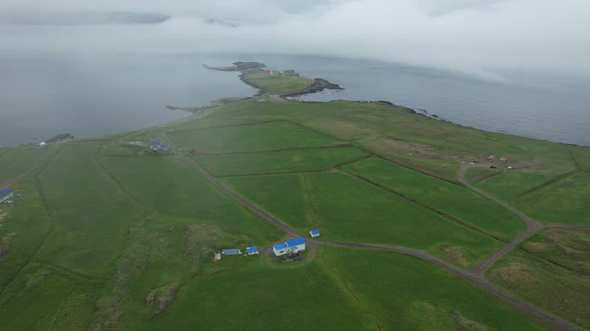 Aerial toward orange lighthouse on Hafnarnes peninsula, Eastfjords Iceland, under an overcast sky, summer