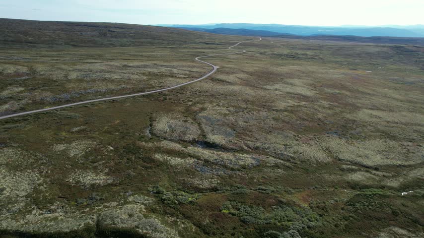 Winding gravel road across mountain plateau, aerial, Ringebu in Ringebufjellet, Innlandet, Norway, filmed with a forward drone flight on a sunny summer day.