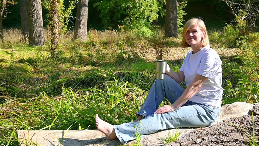 Happy young blonde woman laughing and drinking coffee outdoors slow motion