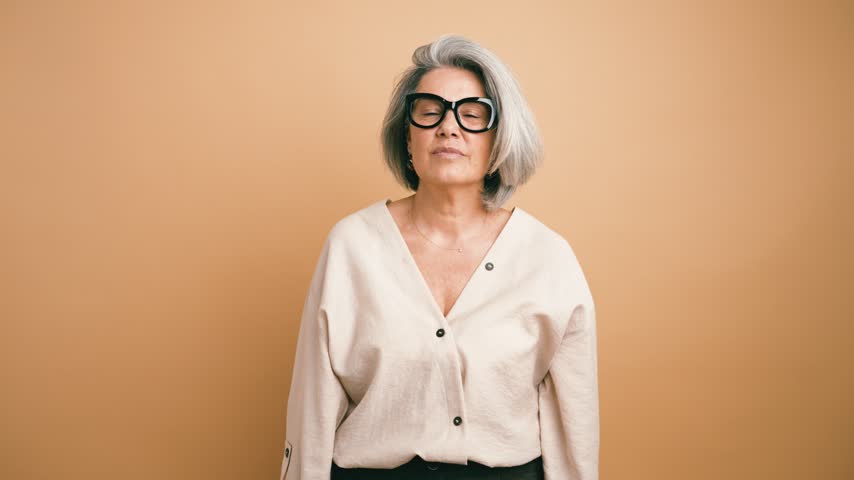 Elegant older woman with grey hair and glasses standing with arms folded. The stylish businesswoman expressing confidence and satisfaction