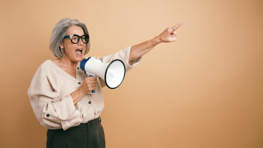 Energetic senior woman with grey hair protesting, shouting into a megaphone. Female leader making an announcement or leading a protest