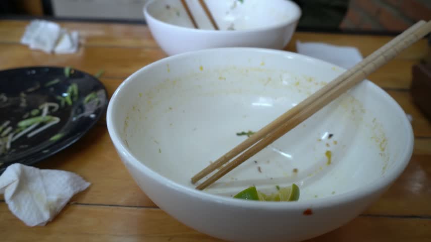 A man finishes his meal with chopsticks. Food and utensils are visible at a restaurant table in Vietnam.