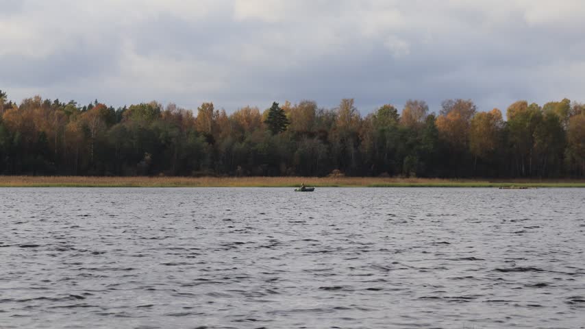 A boat with a fisherman on the river waters on an autumn day