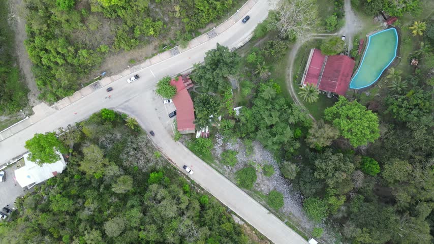 Top down aerial view of a curved road, house, and trees in Guatemala.