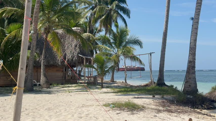 Peaceful tropical Caribbean beach with rustic thatched huts and tall coconut palm trees overlooking calm turquoise ocean water in the San Blas Islands, Panama.