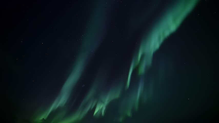 Northern lights aurora borealis ribbons of green light sweeping across starry night sky creating flowing celestial motion and luminous curtains over dark horizon view from ground level nightscape
