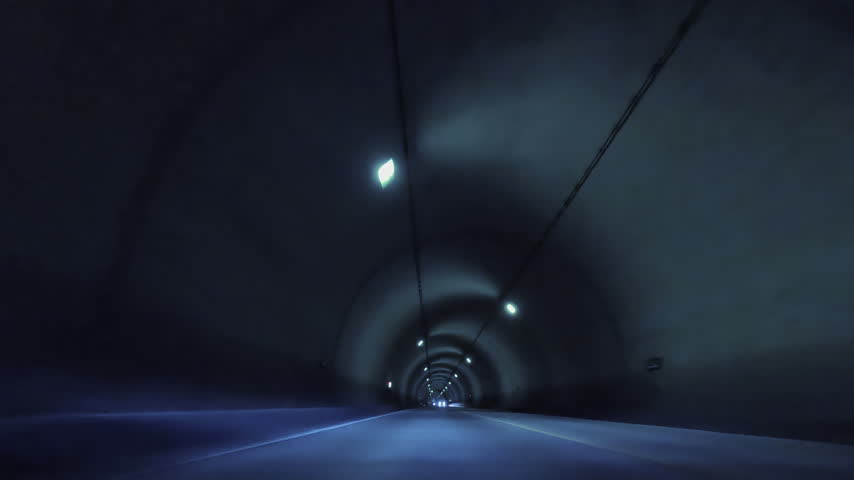 The interior of a quiet tunnel with a line of lights stretching through the darkness, and the view of the road.